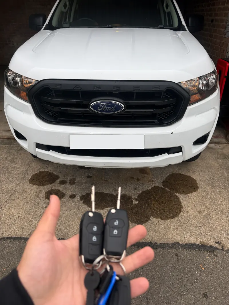 White Ford Ranger pick-up with two black Ford remote flip keys held in front of it, number plate obscured