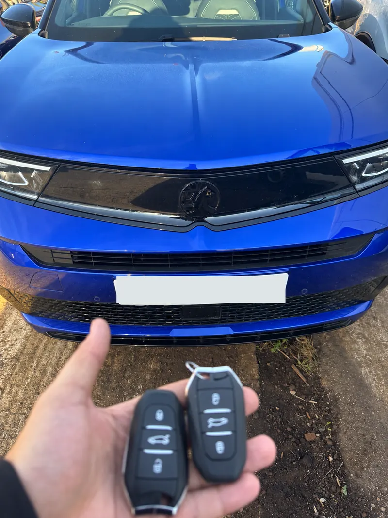 Blue Vauxhall car with two black remote key fobs held in front of it, number plate obscured